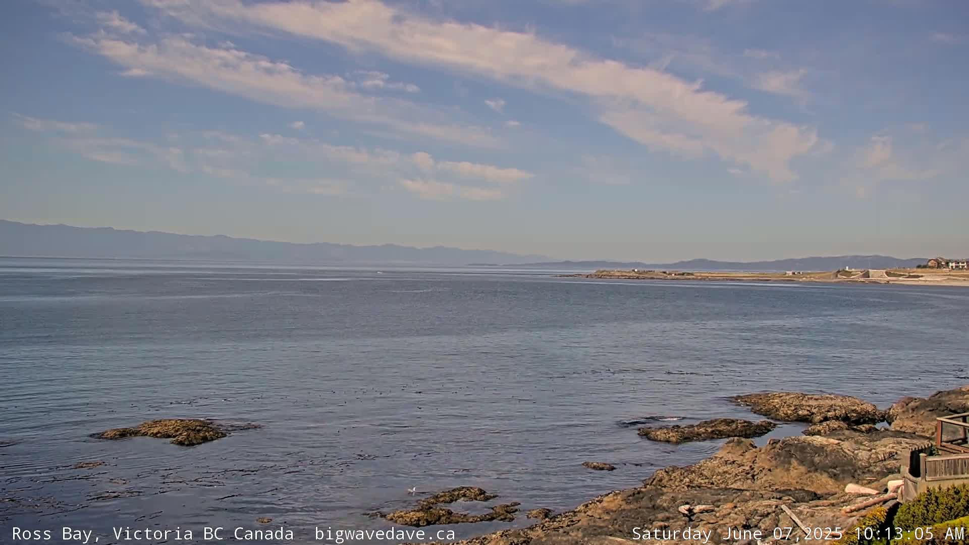 A calm bay with rocky shores and distant mountains under a partly cloudy sky.