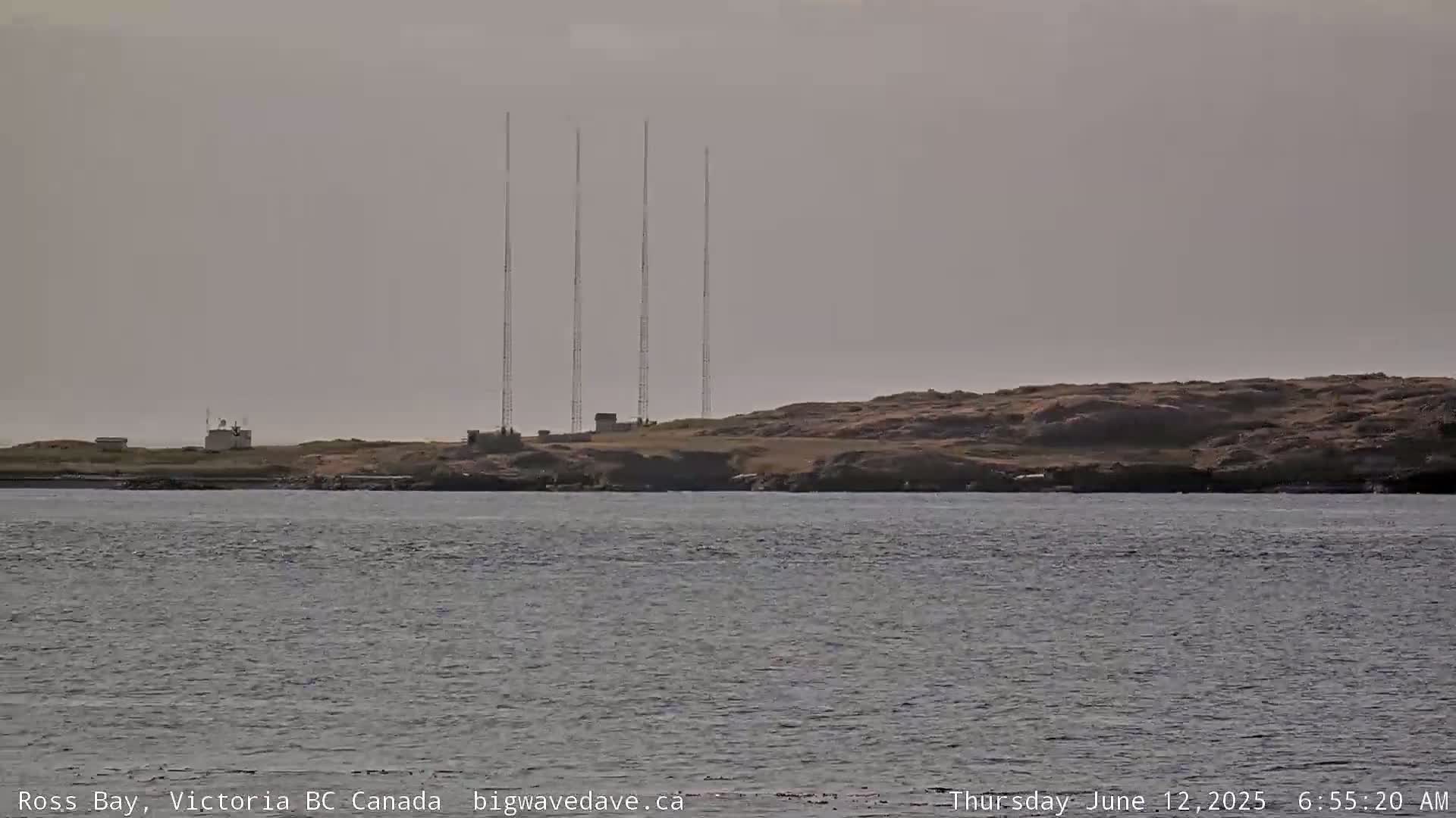 Across calm water, a rocky shoreline is visible, featuring several tall antenna towers on a small, flat area.