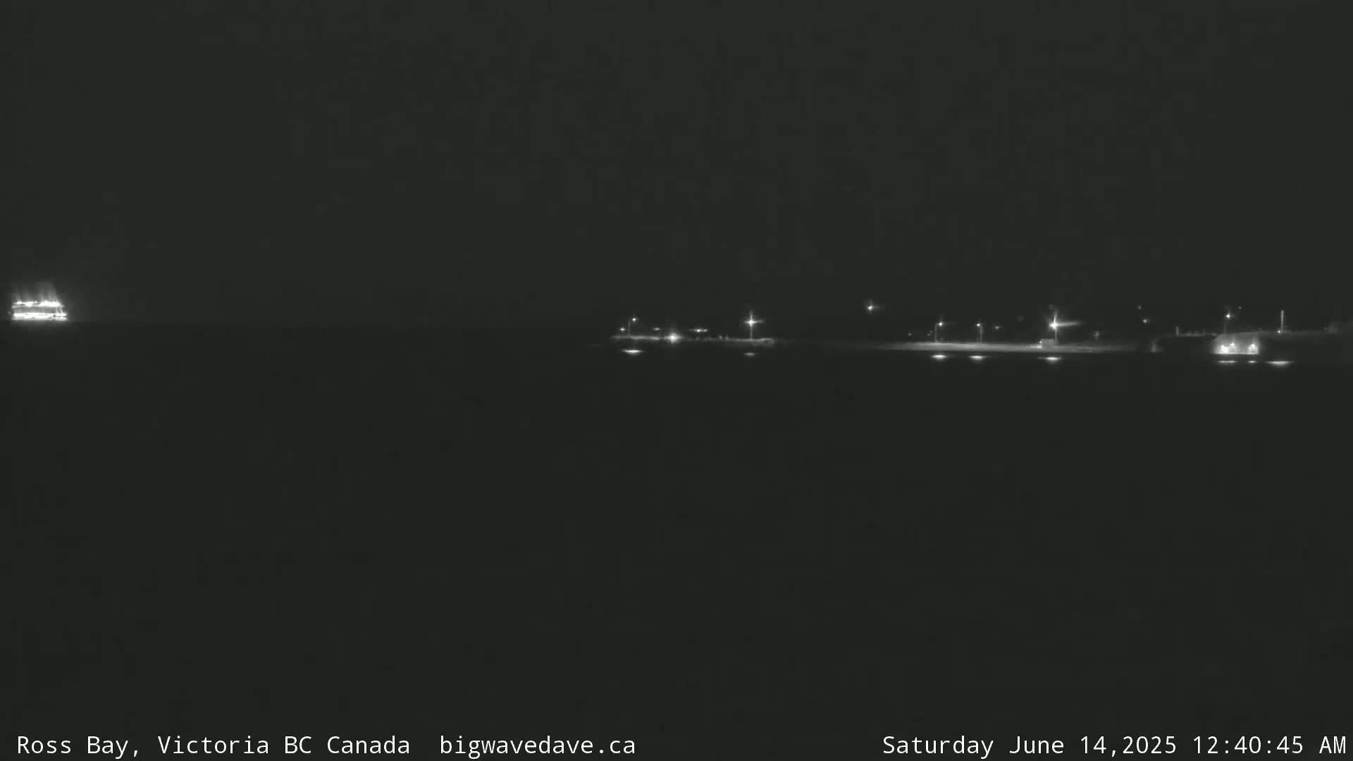 A dimly lit body of water at night with a distant vessel and shoreline lights visible.