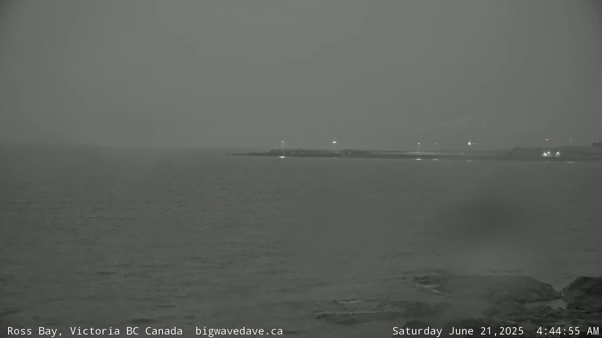 A hazy, dark view of a calm body of water with a distant shoreline at night.