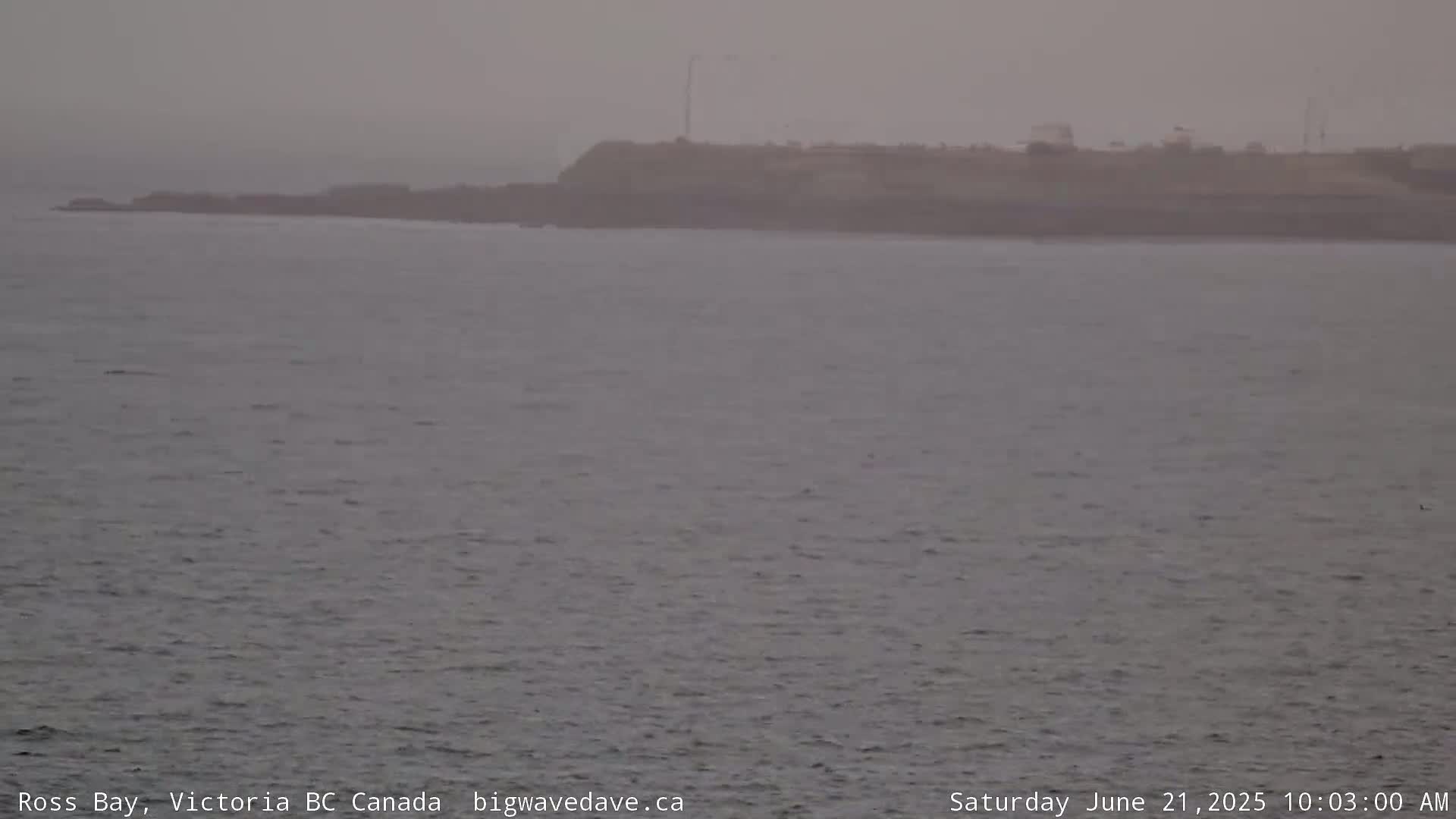 A hazy, overcast view shows a dark landmass extending across the horizon over a calm body of water.