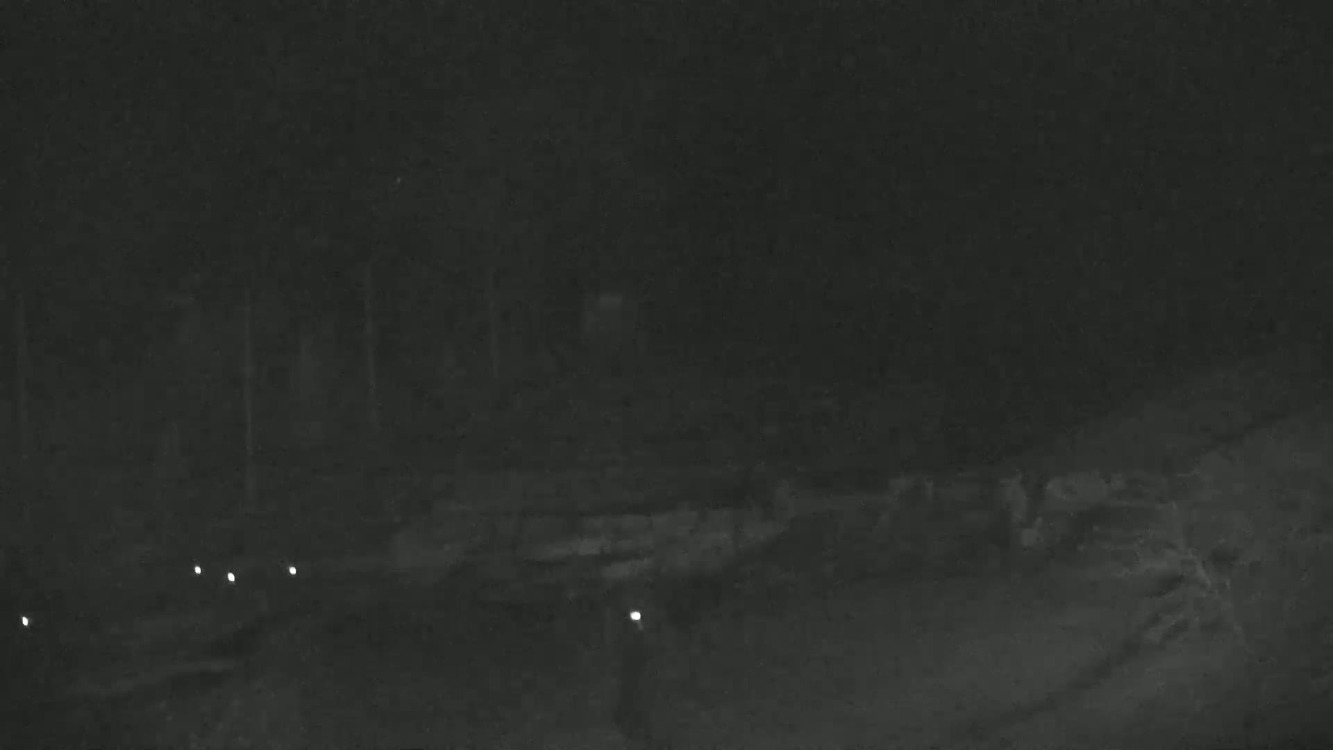 A dark, nighttime scene shows a dimly lit area with faint shapes and several small lights in the distance.