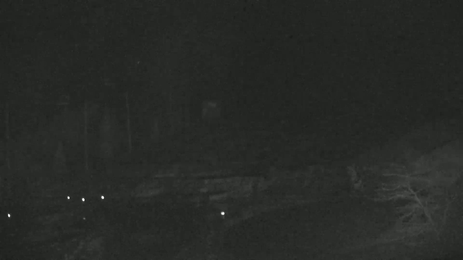 A dark, nighttime scene shows a blurry, indistinct landscape with several small, bright lights in the lower portion of the image.
