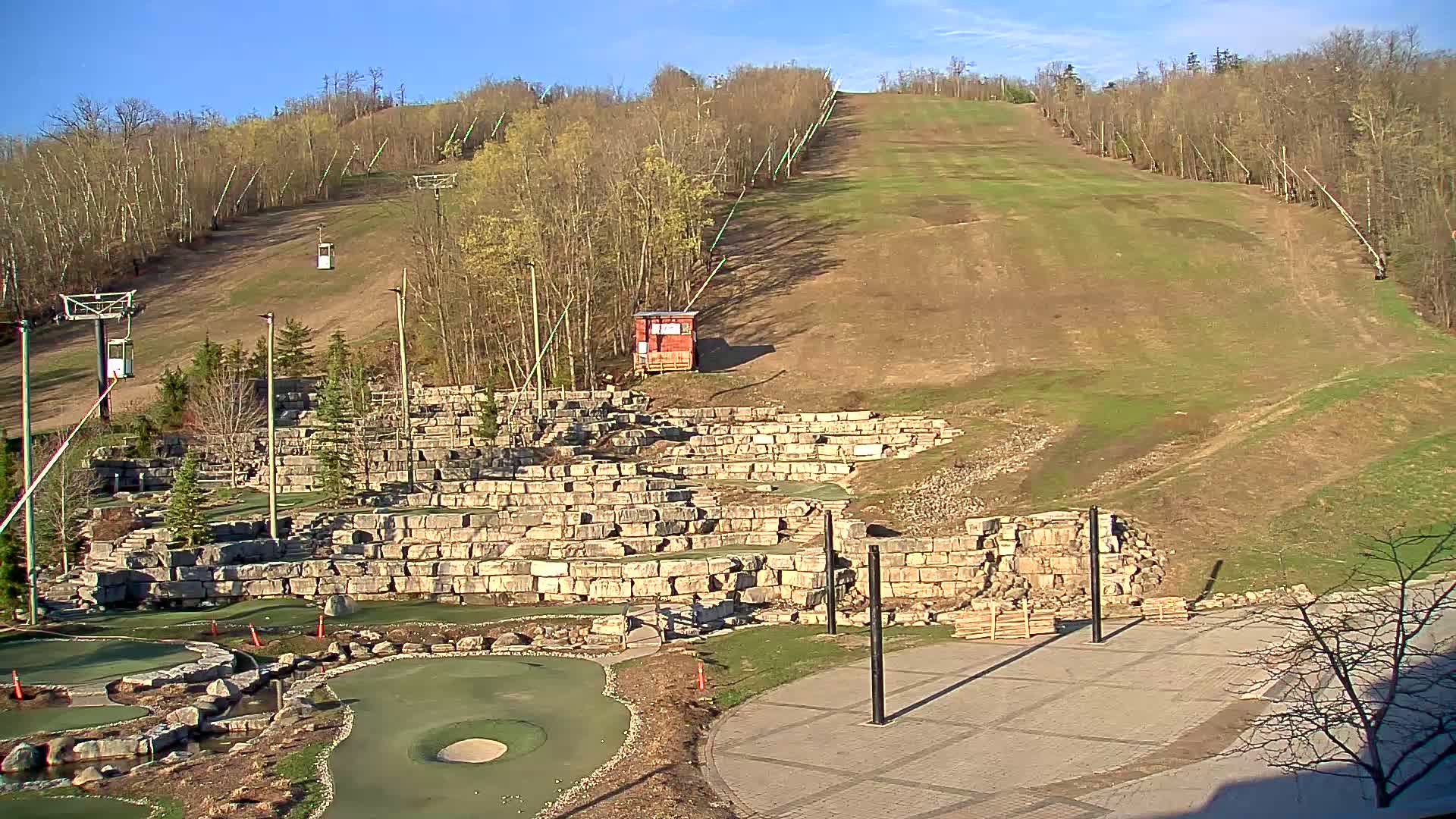 A grassy ski slope with chairlifts and a stone mini-golf course sits below it on a sunny day.