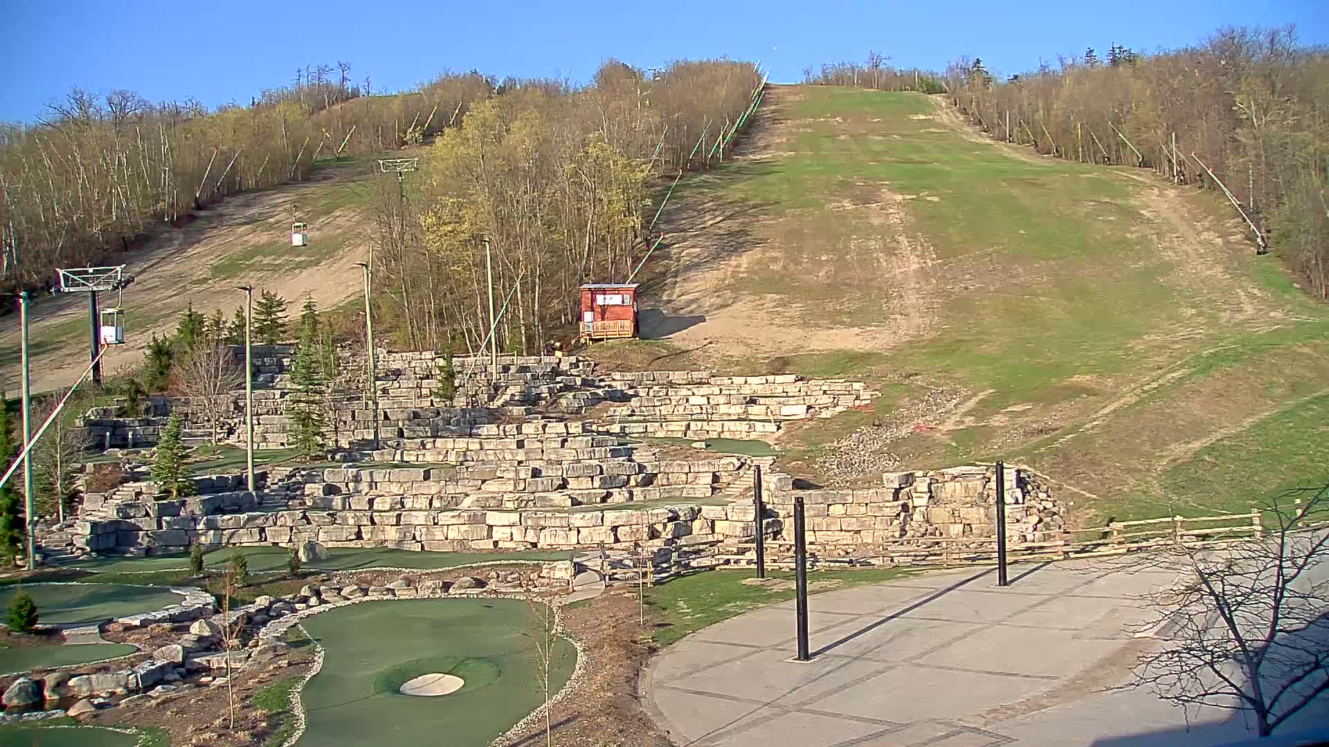 A grassy ski slope with chairlifts and a stone mini-golf course below, under a clear blue sky.