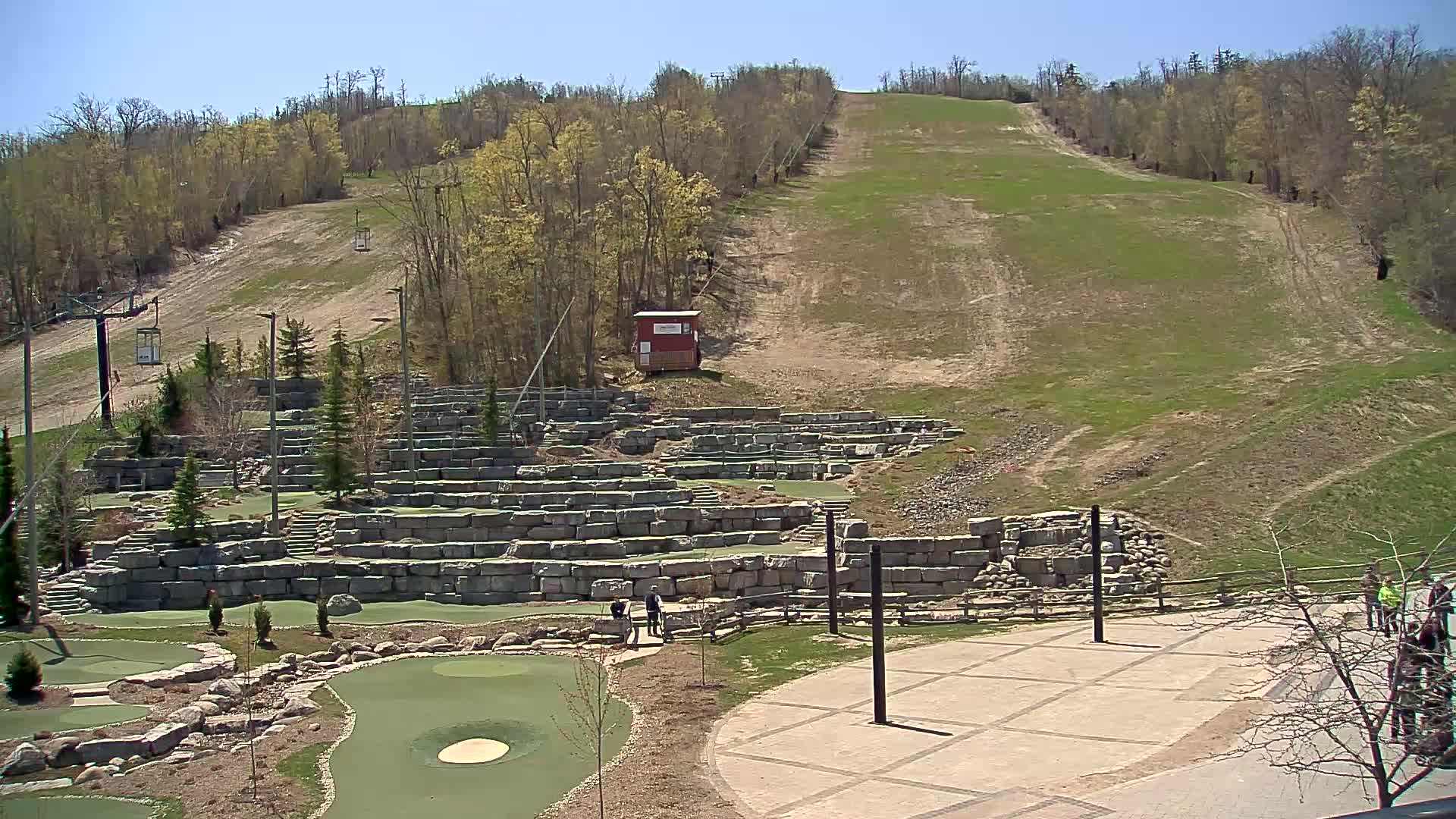 A grassy ski slope overlooks a stone mini-golf course on a sunny day.