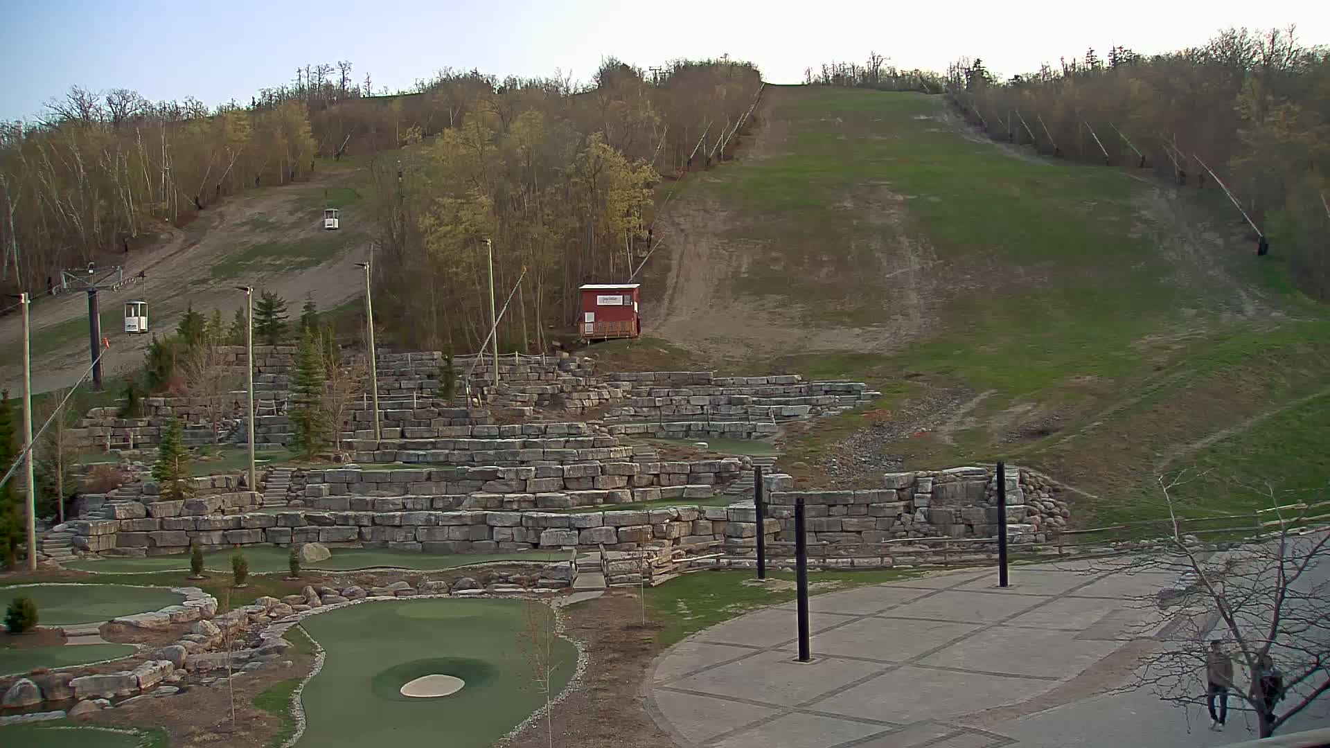 A grassy hillside with a ski lift and a stone-walled mini-golf course below, under a clear evening sky.