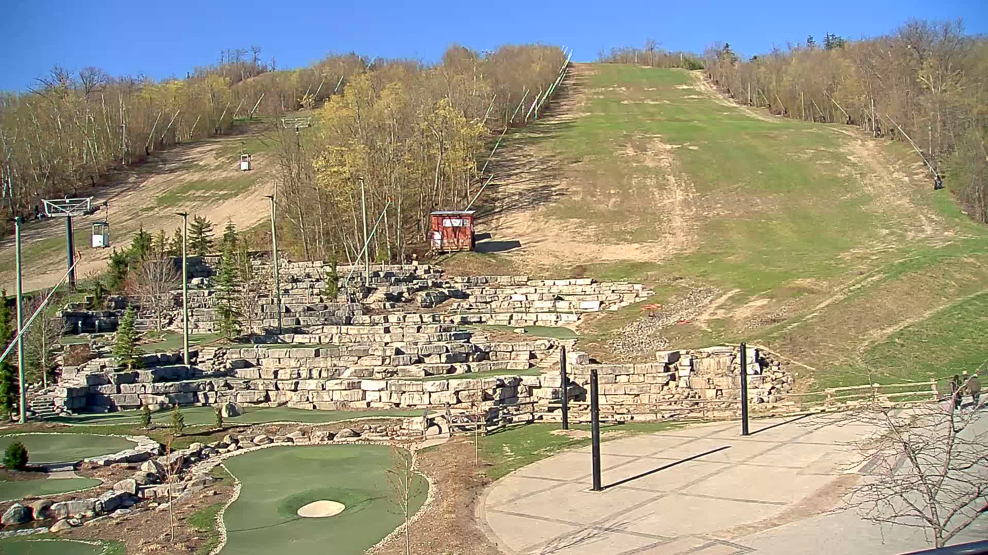 A grassy hill with a ski lift, a stone mini-golf course, and a paved area is visible on a sunny day.