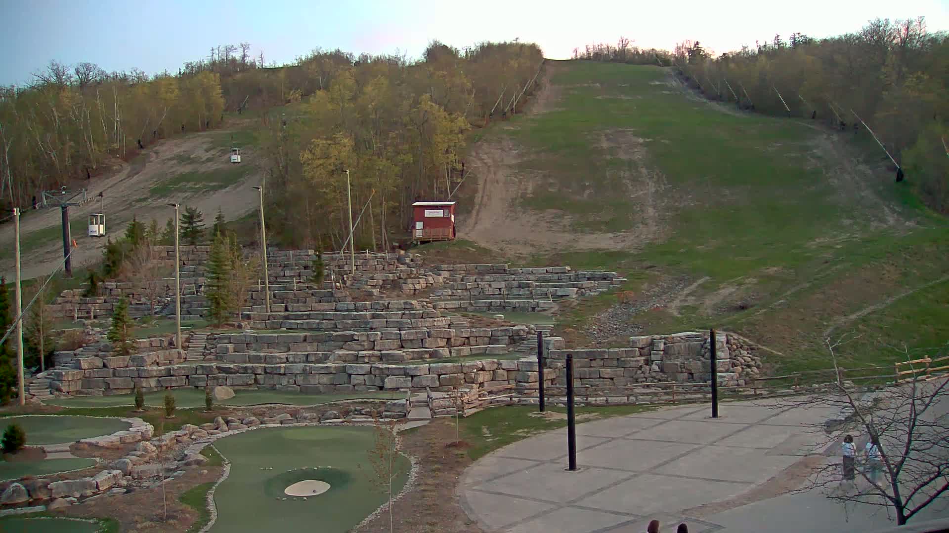A grassy ski slope with chairlifts and a stone mini-golf course below it, under a clear evening sky.