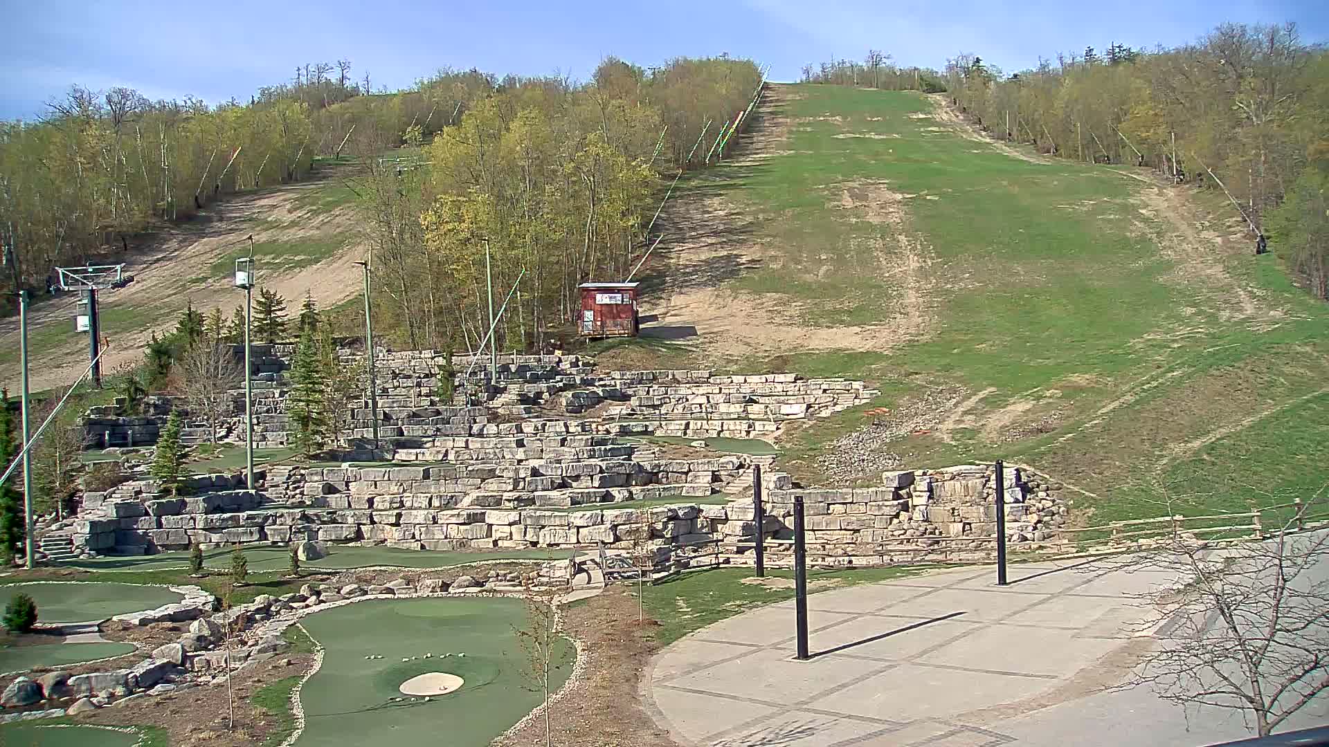 A grassy hill with a ski lift, a miniature golf course built into stone retaining walls, and a paved area are visible on a clear, sunny day.