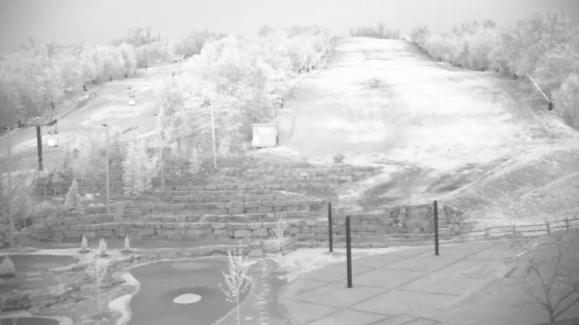 A snow-covered ski slope with a chairlift and a miniature golf course below, on an overcast day.