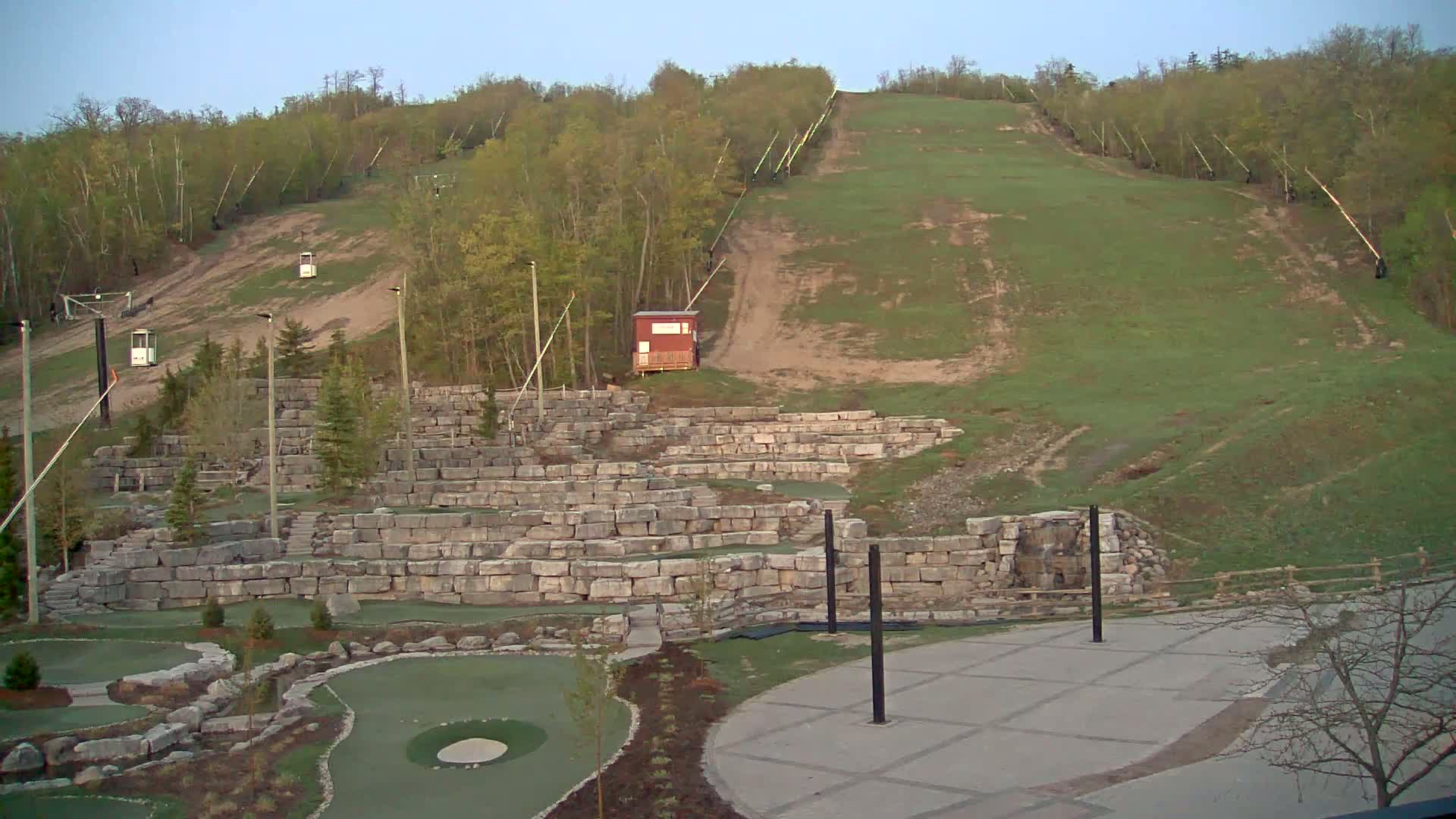 A grassy hill with ski lift infrastructure, a small red building, and a stone-walled miniature golf course are visible under a clear sky.