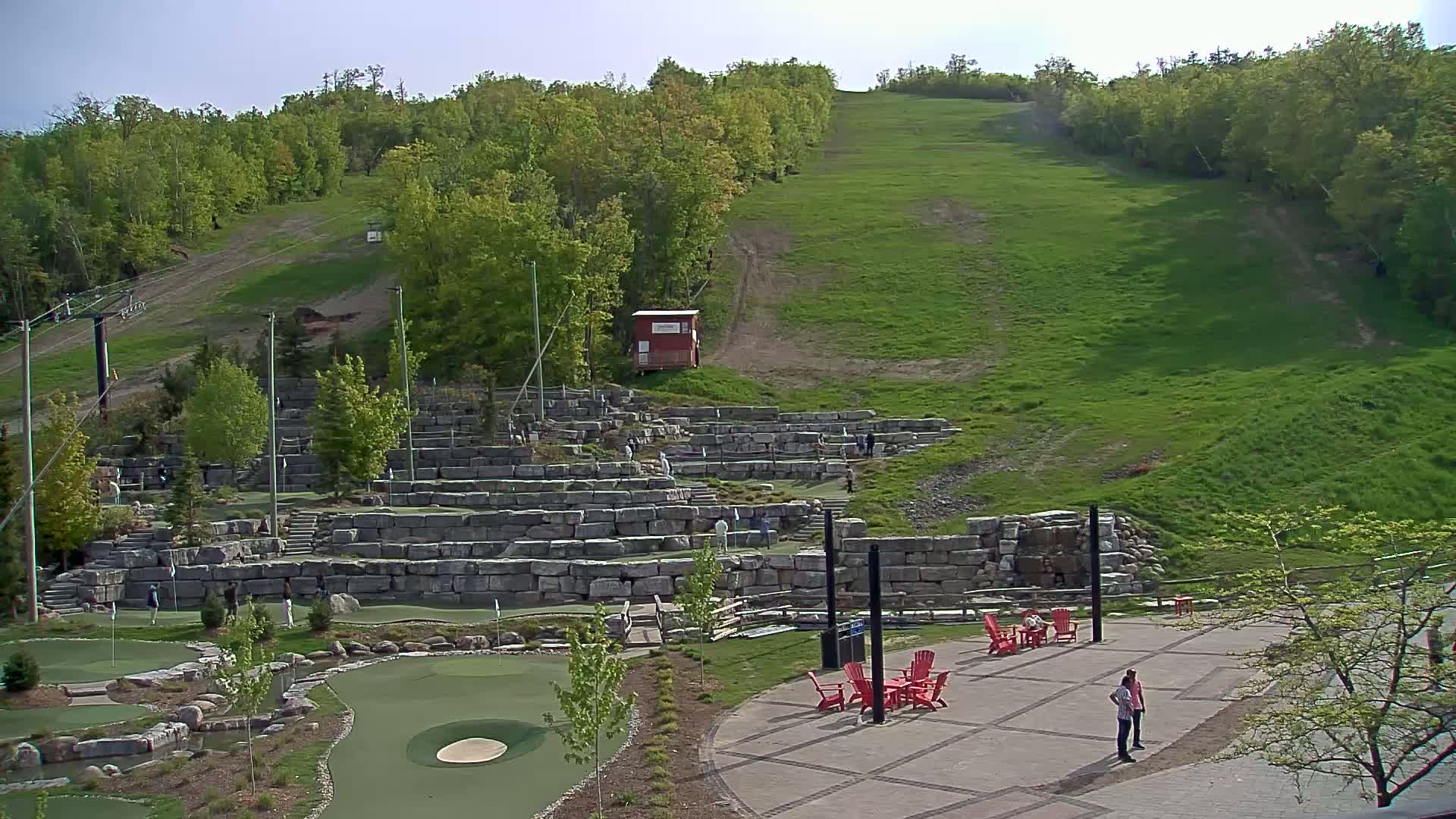 A grassy hillside with a stone mini-golf course and patio area is visible on a sunny day.
