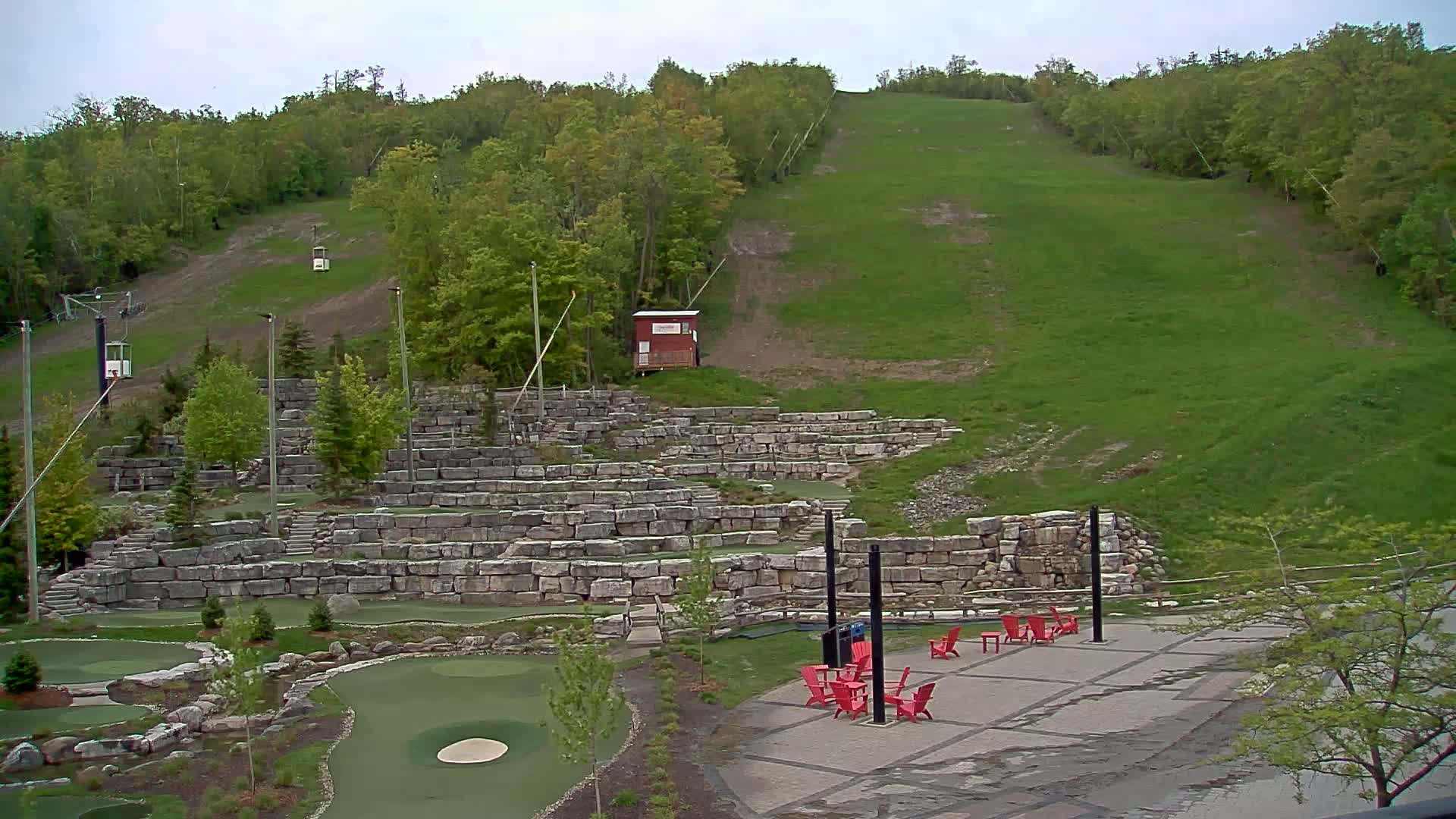 A grassy hill with a ski lift and stone retaining walls forming a mini golf course is visible under an overcast sky.
