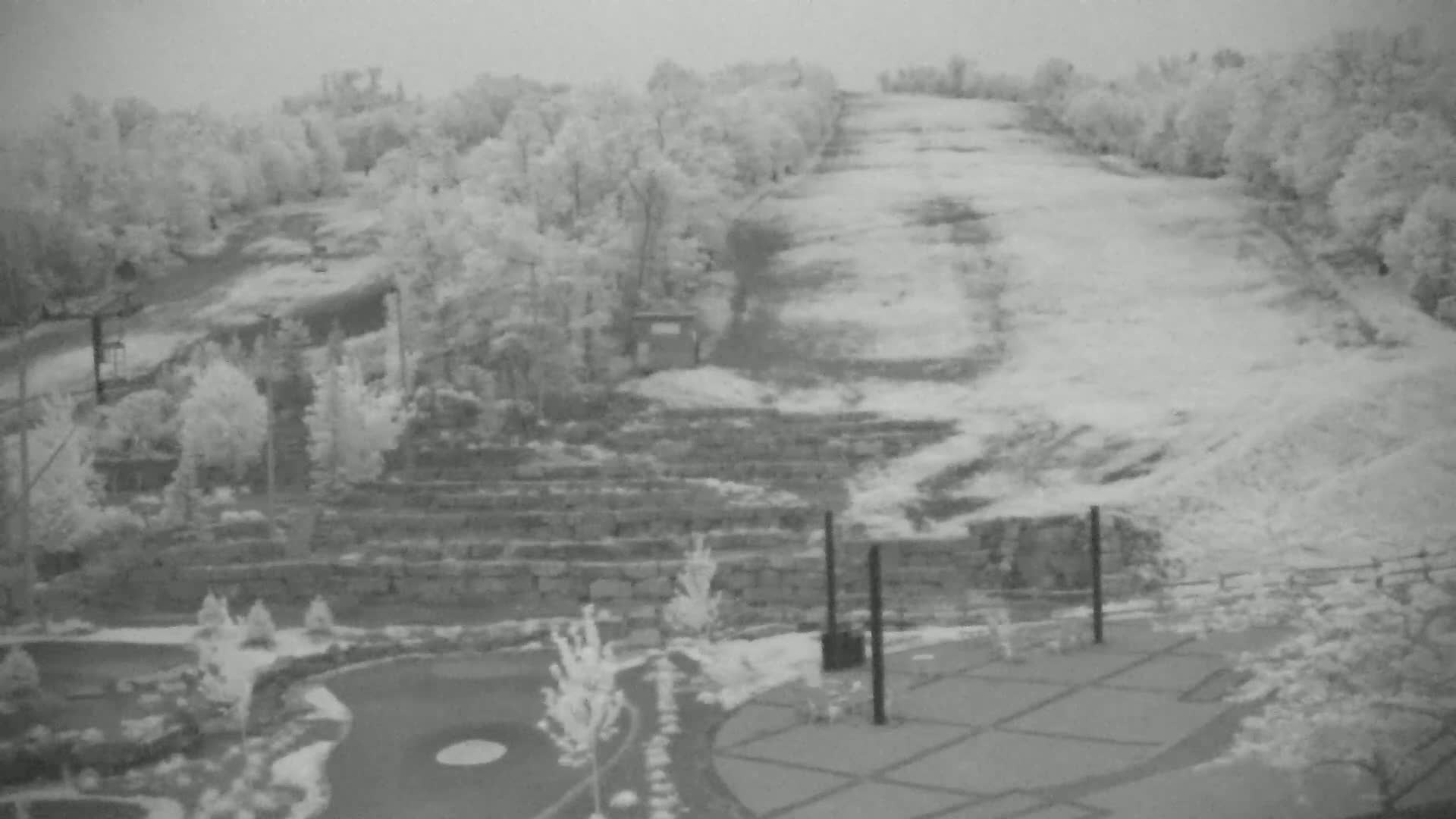 A snow-covered hill with trees and landscaping is viewed from above on an overcast day.