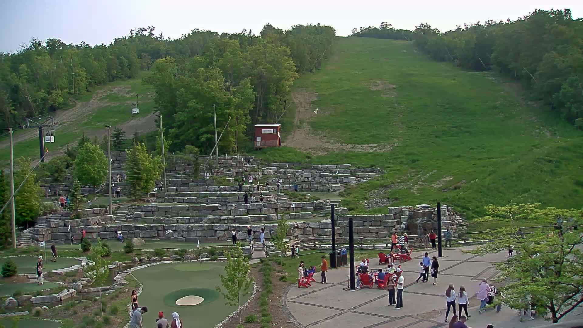 A grassy hill overlooks a stone mini-golf course with many people enjoying the sunny day.