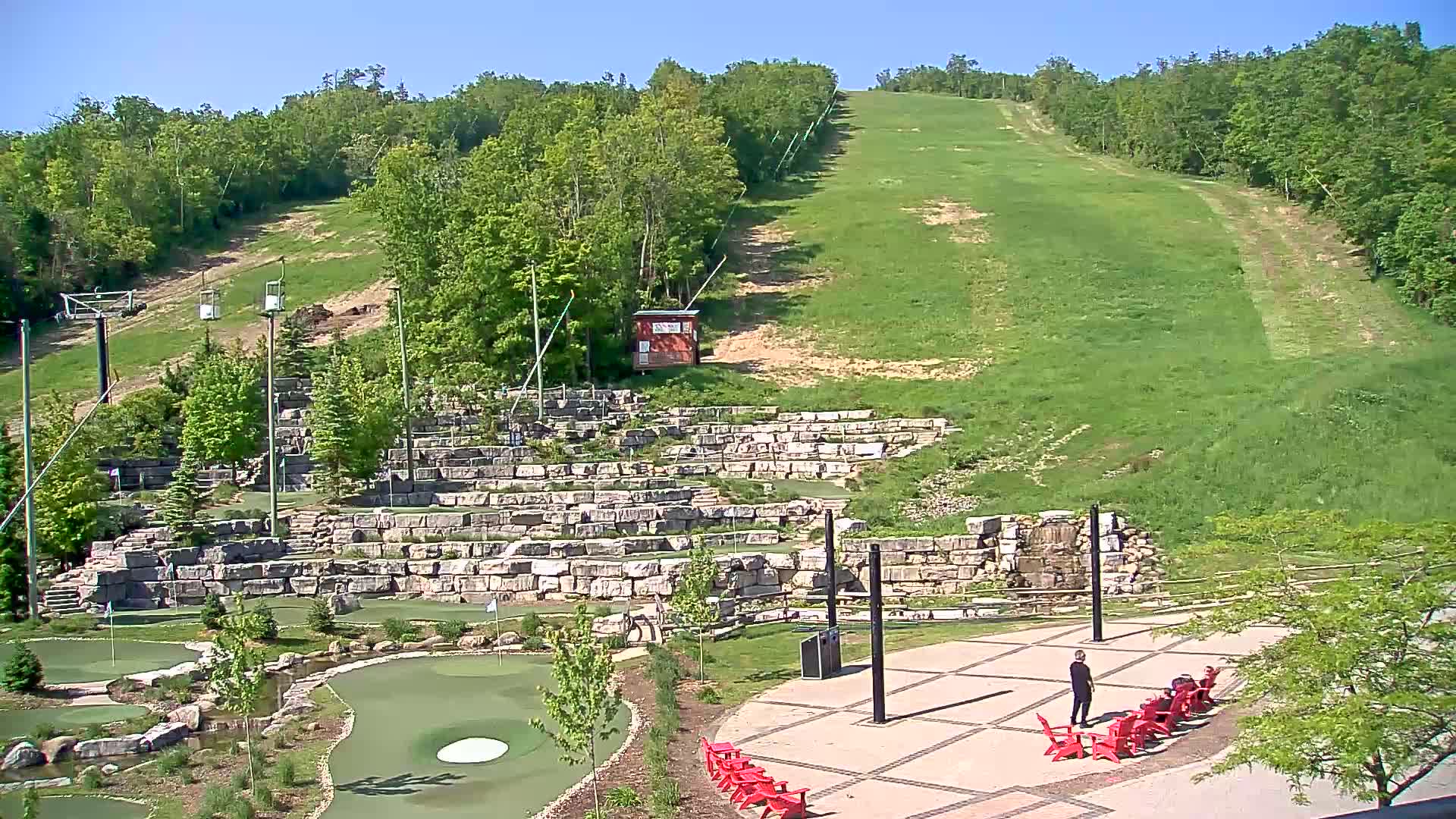 A grassy hillside with a ski lift and a mini golf course below on a sunny day.
