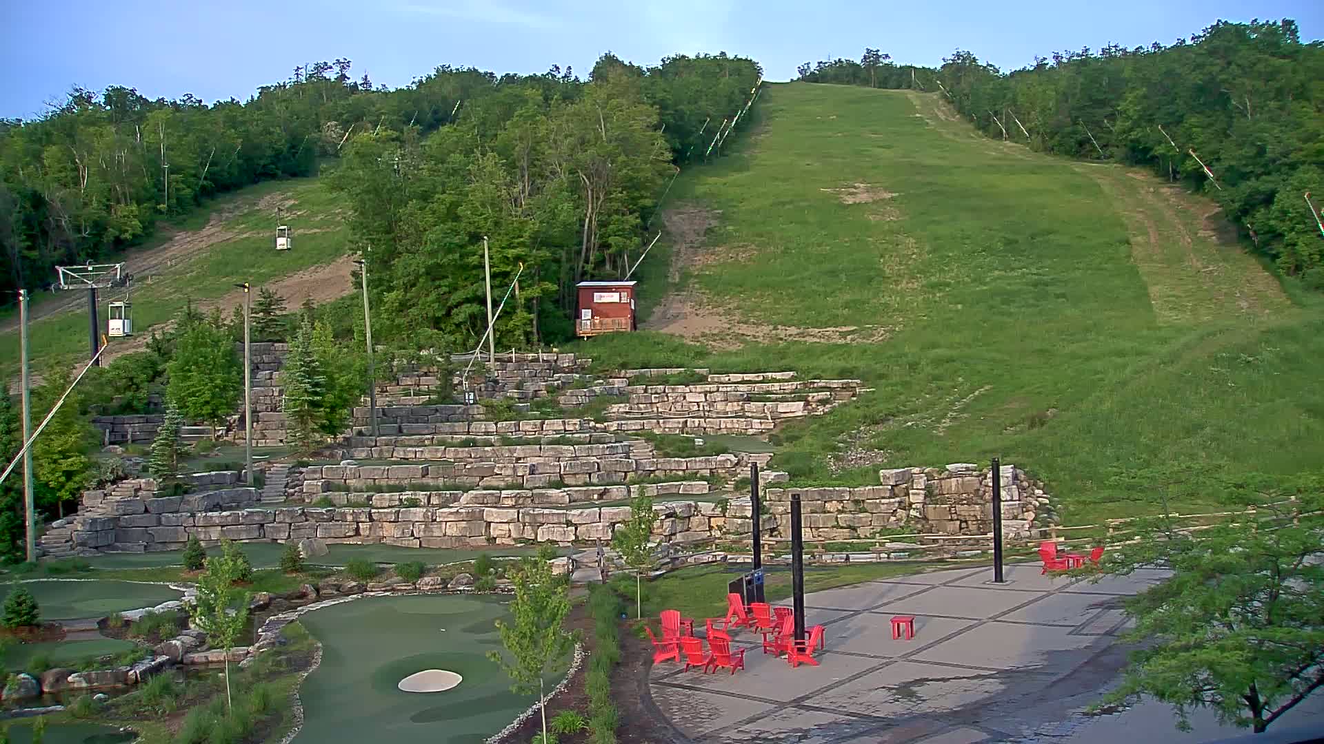 A grassy ski hill with a chairlift and a stone amphitheater-like structure at the base, under a mostly clear sky.
