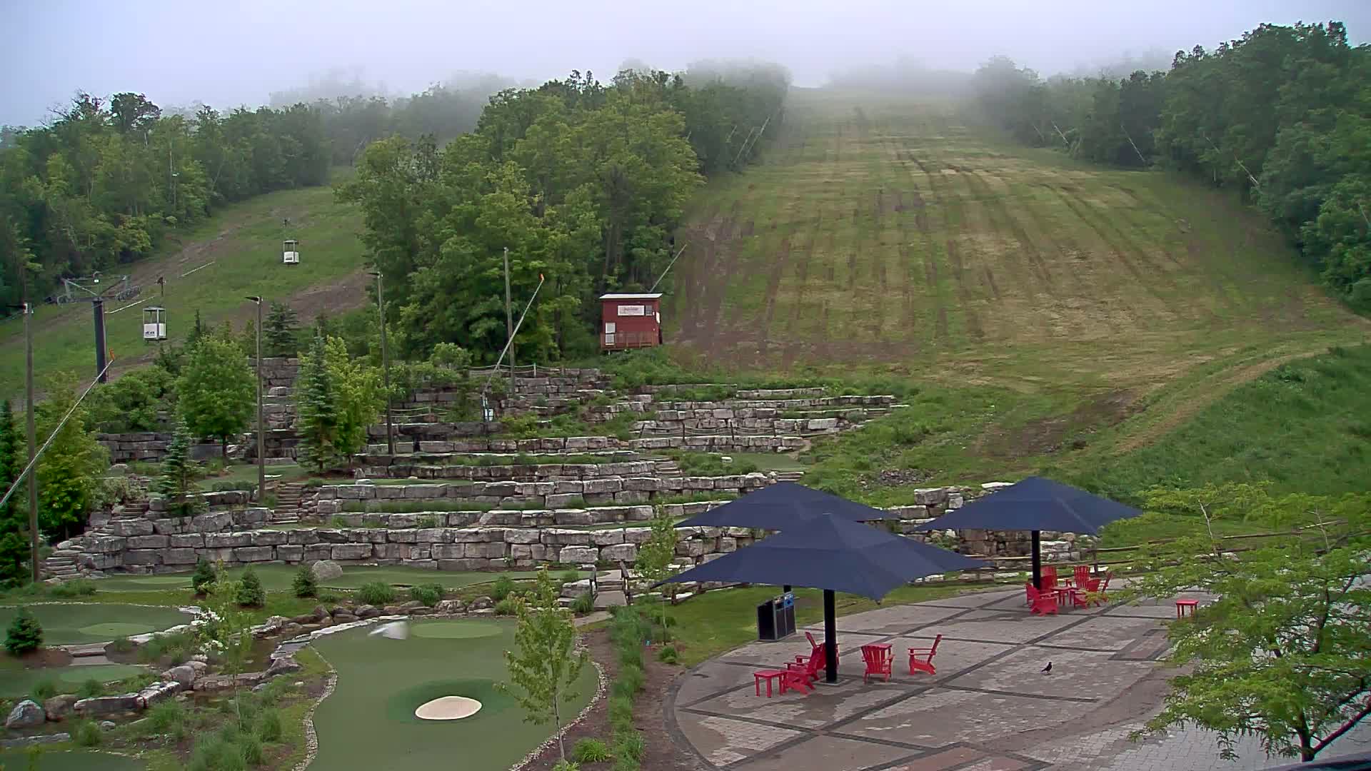 A grassy hill with a chairlift and a mini golf course below, all under a foggy sky.