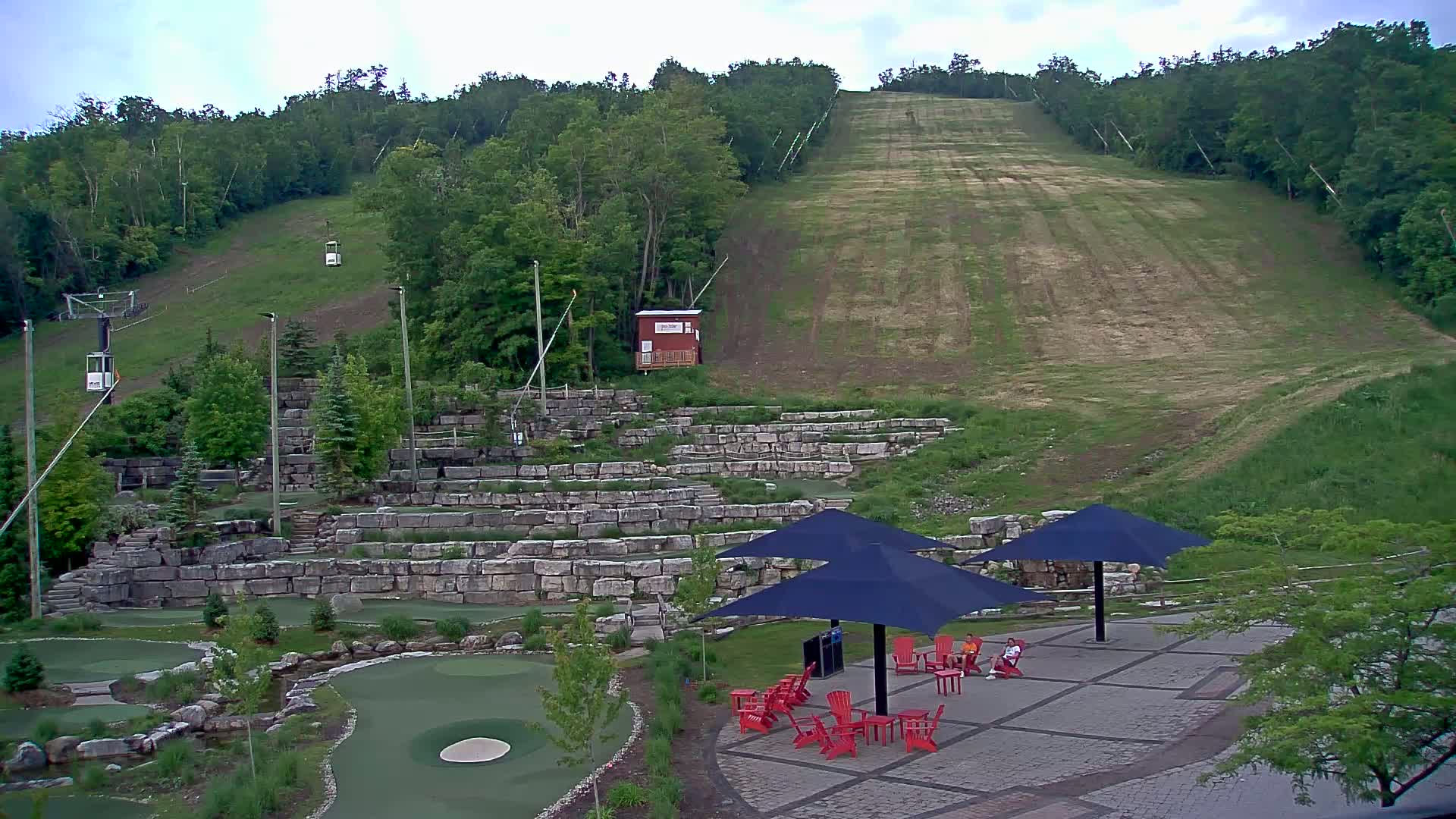 A grassy hillside with a ski lift and a miniature golf course below, under an overcast sky.