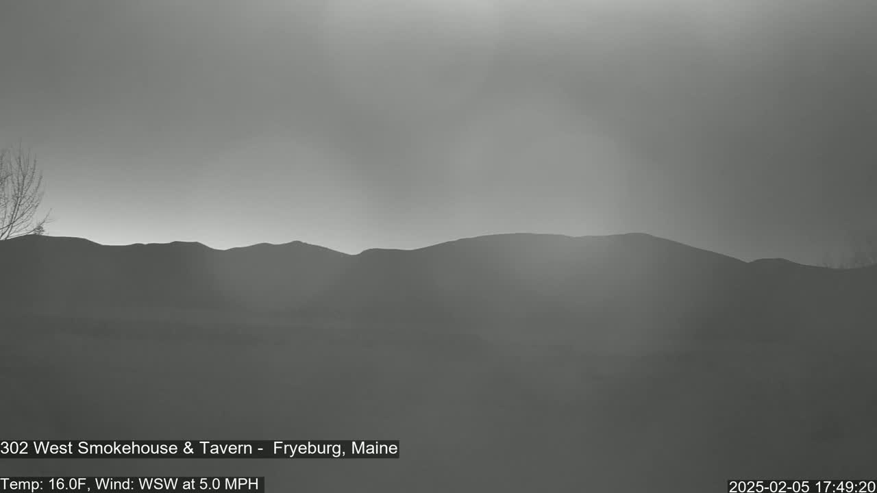 A hazy, grayscale view shows a range of dark, distant hills under a pale sky, with a light wind.