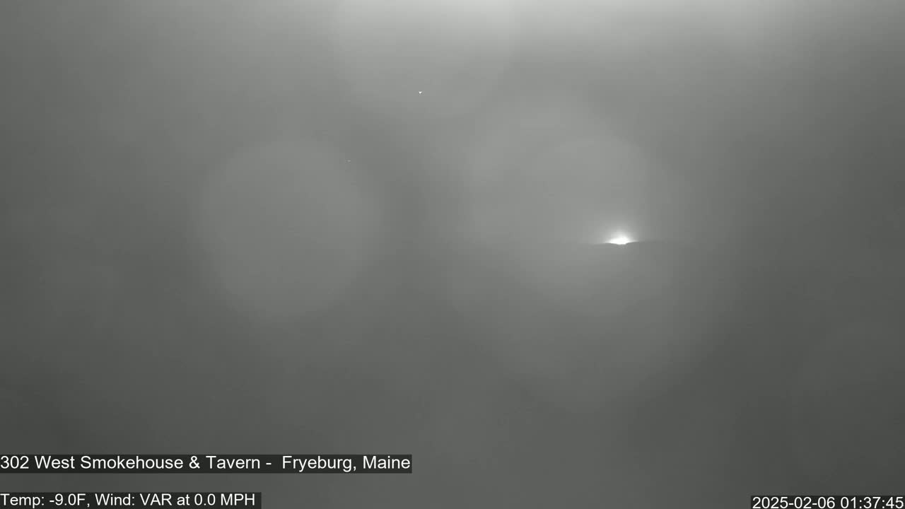 A hazy, low-light outdoor scene shows a distant, bright light possibly a sunrise or sunset, under a foggy sky.