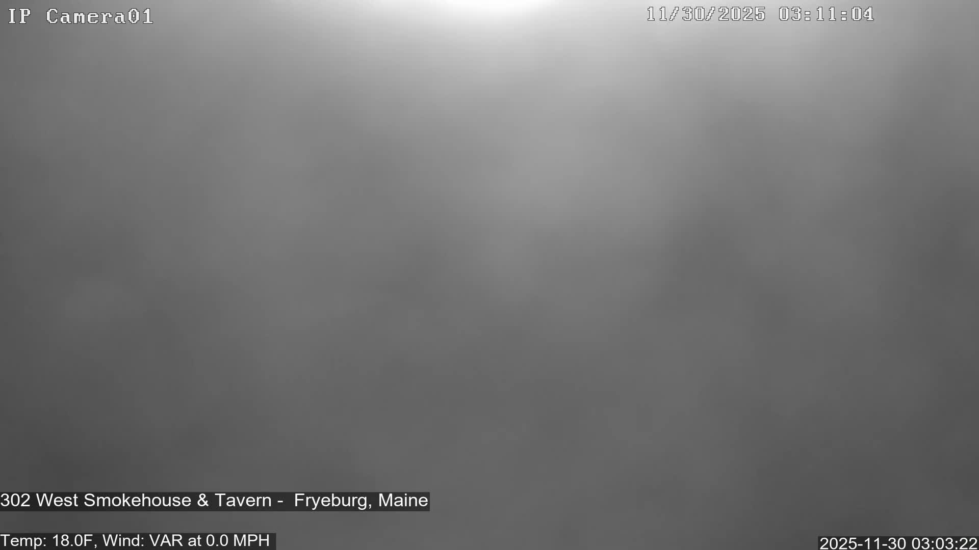 The image displays an outdoor scene completely obscured by extremely dense fog or heavy overcast conditions, presenting as a uniform field of grey with a bright, diffused light source barely visible at the top.