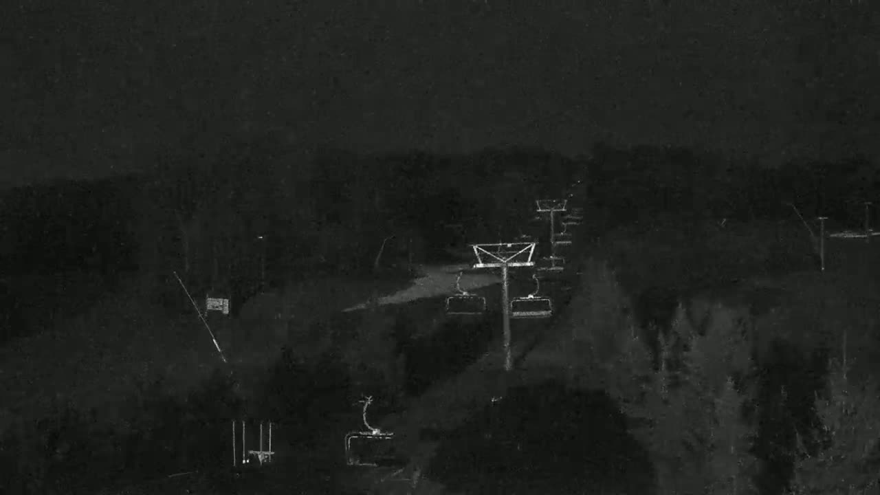 A nighttime, low-light view of a ski lift against a dark, wooded landscape.