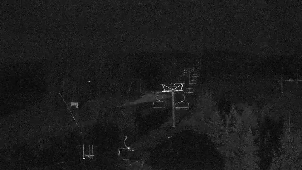 A nighttime, low-light view of a ski lift and surrounding trees.