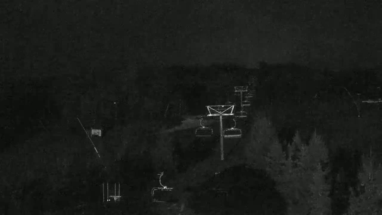 A nighttime, low-light view of a ski lift ascending a dark, wooded hillside.