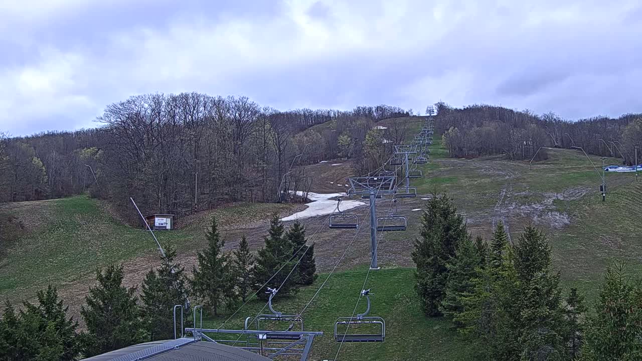An empty ski lift ascends a grassy hill under a cloudy sky.