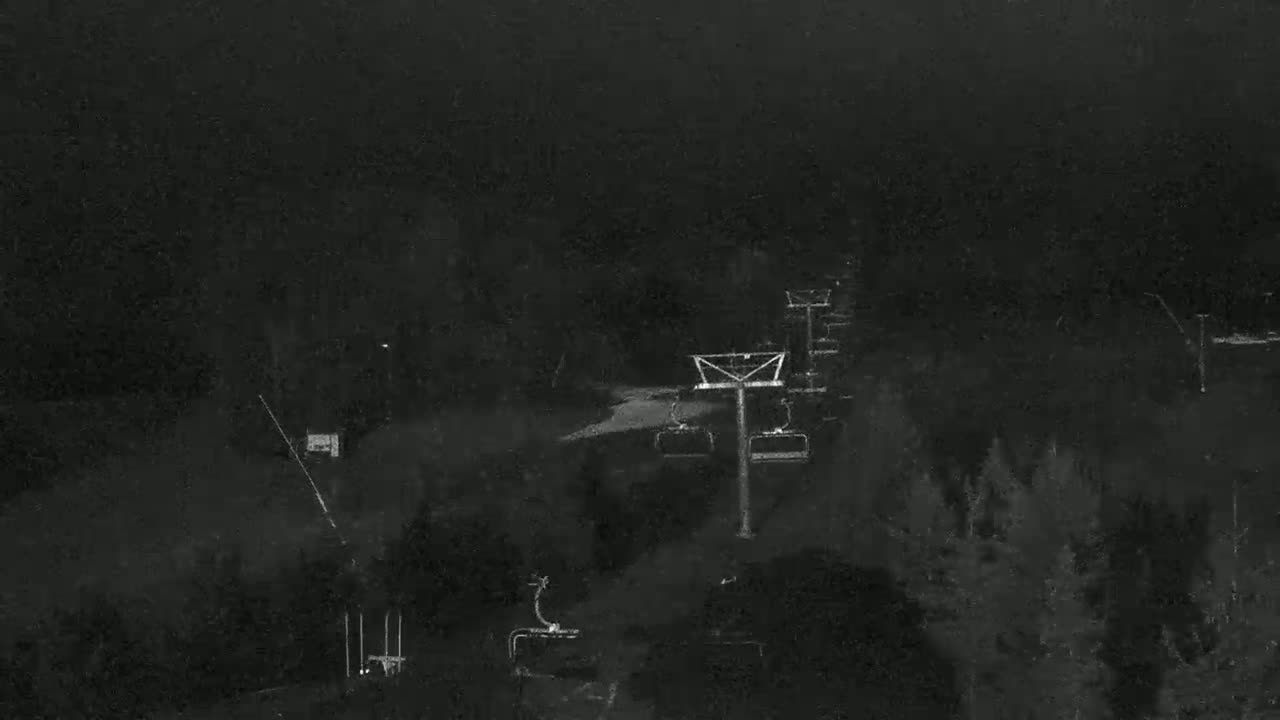 A nighttime, low-light image shows a ski lift and surrounding trees under a dark, possibly cloudy sky.