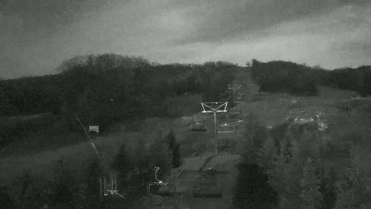 A chairlift ascends a sparsely wooded hill under a dark, overcast sky.