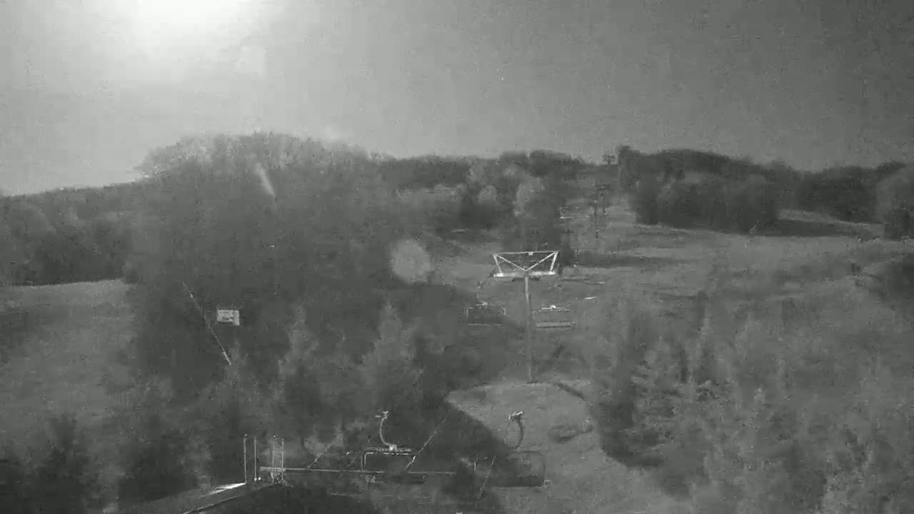 A hazy, bright day shows a ski lift and surrounding treeline in a mostly barren landscape.
