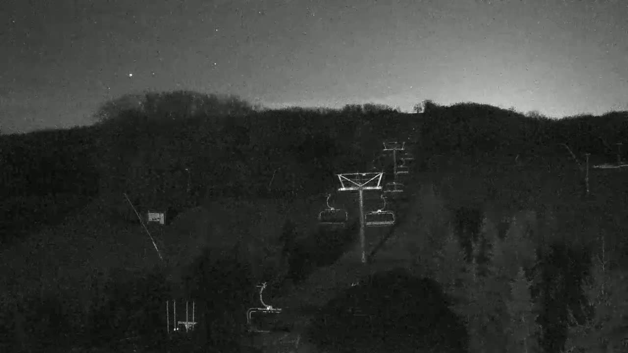 A ski lift ascends a dark, tree-covered hill under a night sky.