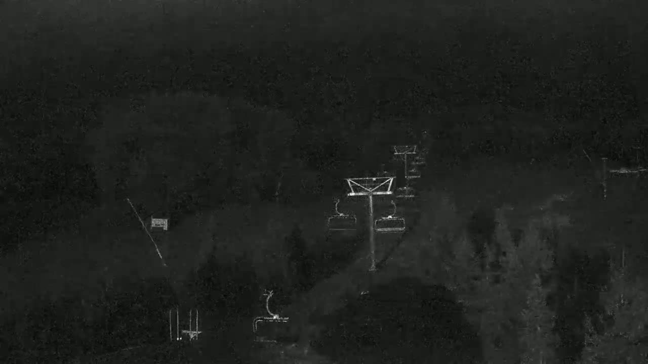 A nighttime, low-light image shows a ski lift against a dark, wooded background.