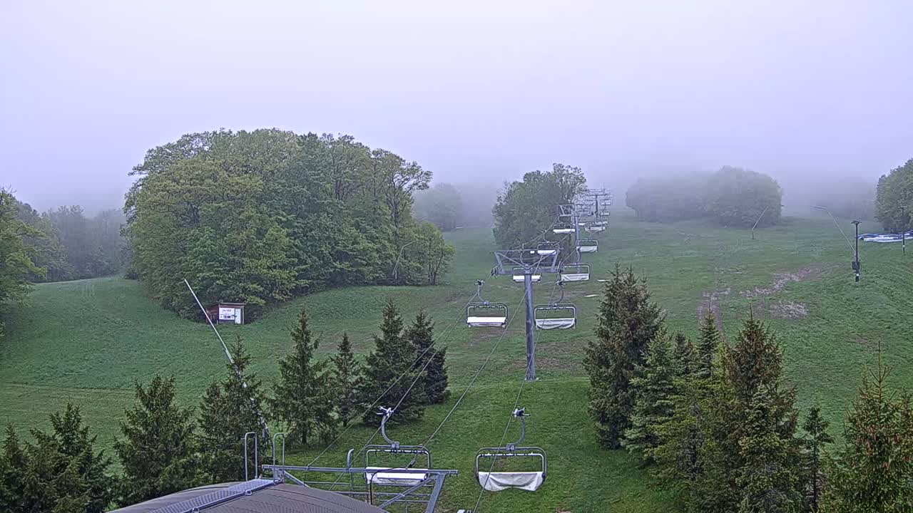 A chairlift extends across a grassy hill surrounded by fog-covered trees.