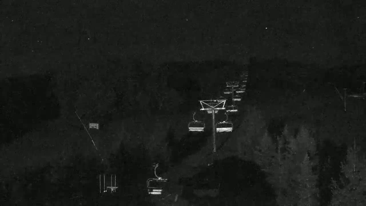 A nighttime, low-light image shows a chairlift ascending a dark, wooded hill under a starlit sky.