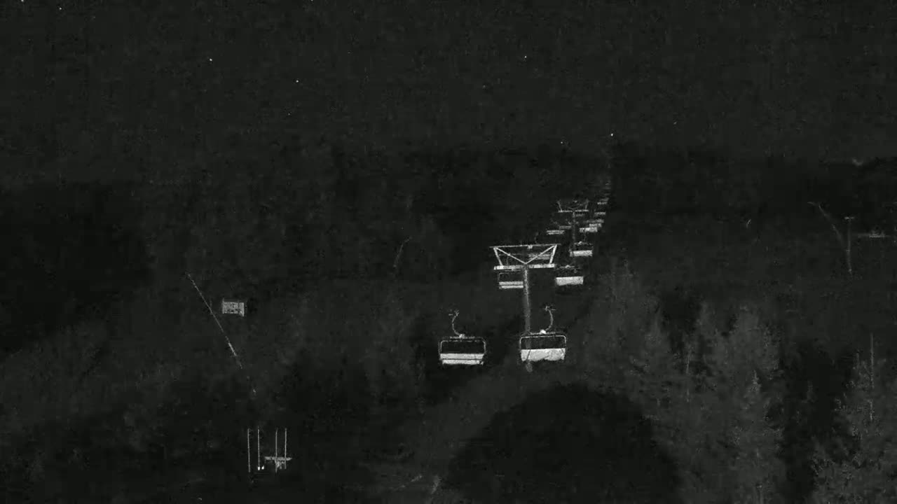 A nighttime, low-light view of a chairlift ascending a dark, snow-covered slope.