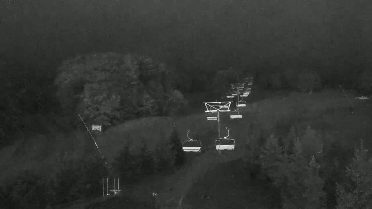 An aerial view shows a chairlift ascending a foggy, wooded hillside.