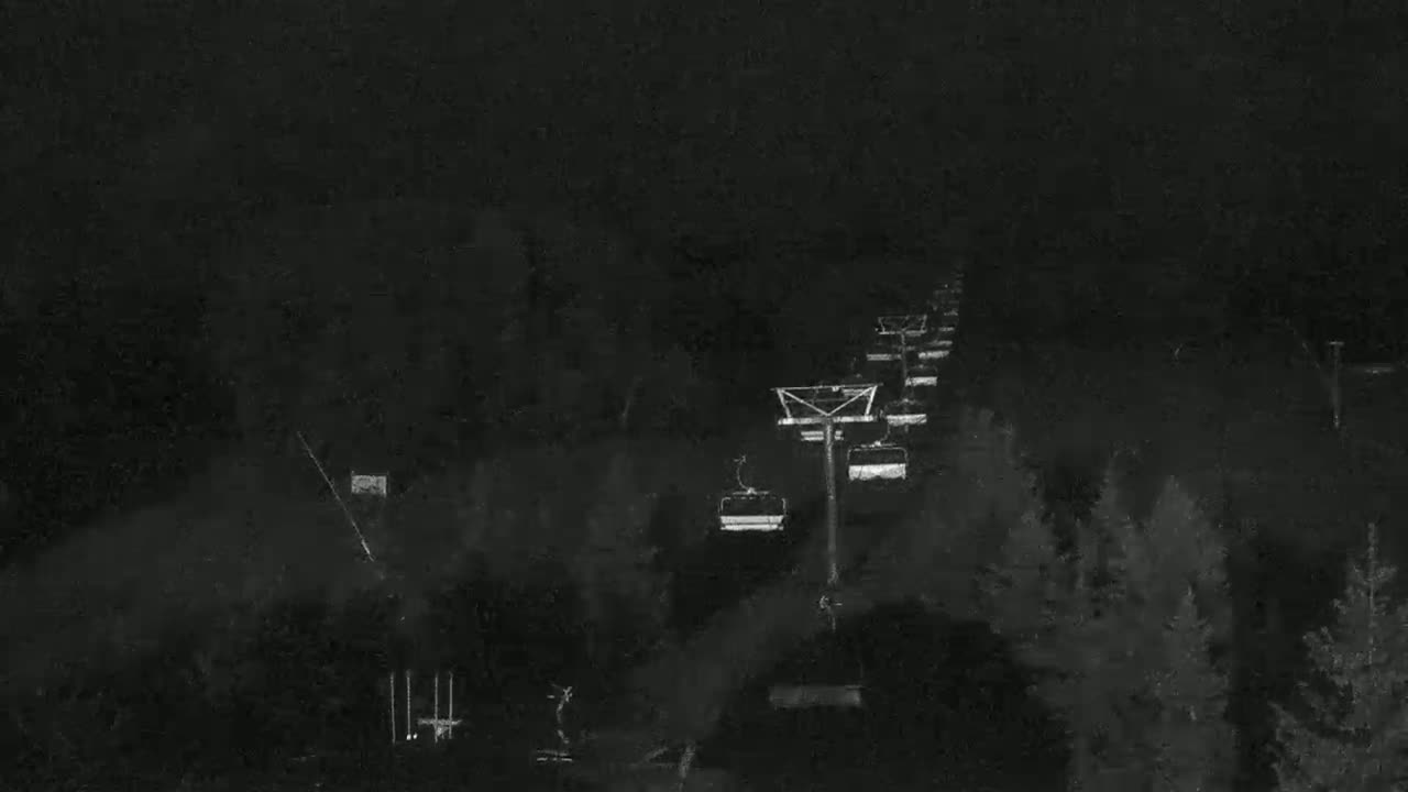 A nighttime, low-light image shows a chairlift ascending a dark, snow-covered mountain slope.