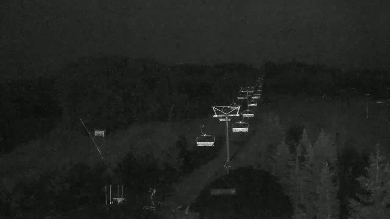 A nighttime view of a chairlift ascending a snow-covered hill under a dark, possibly snowy sky.