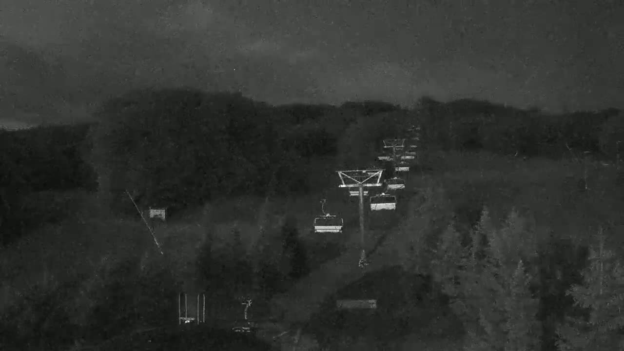 A chairlift ascends a dark, wooded hillside under a cloudy, nighttime sky.