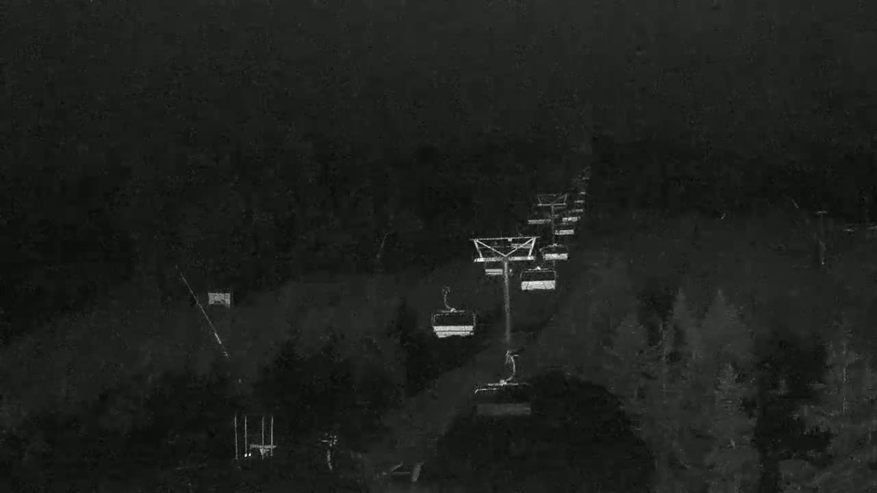 A chairlift ascends a dark, snow-covered mountain slope at night.