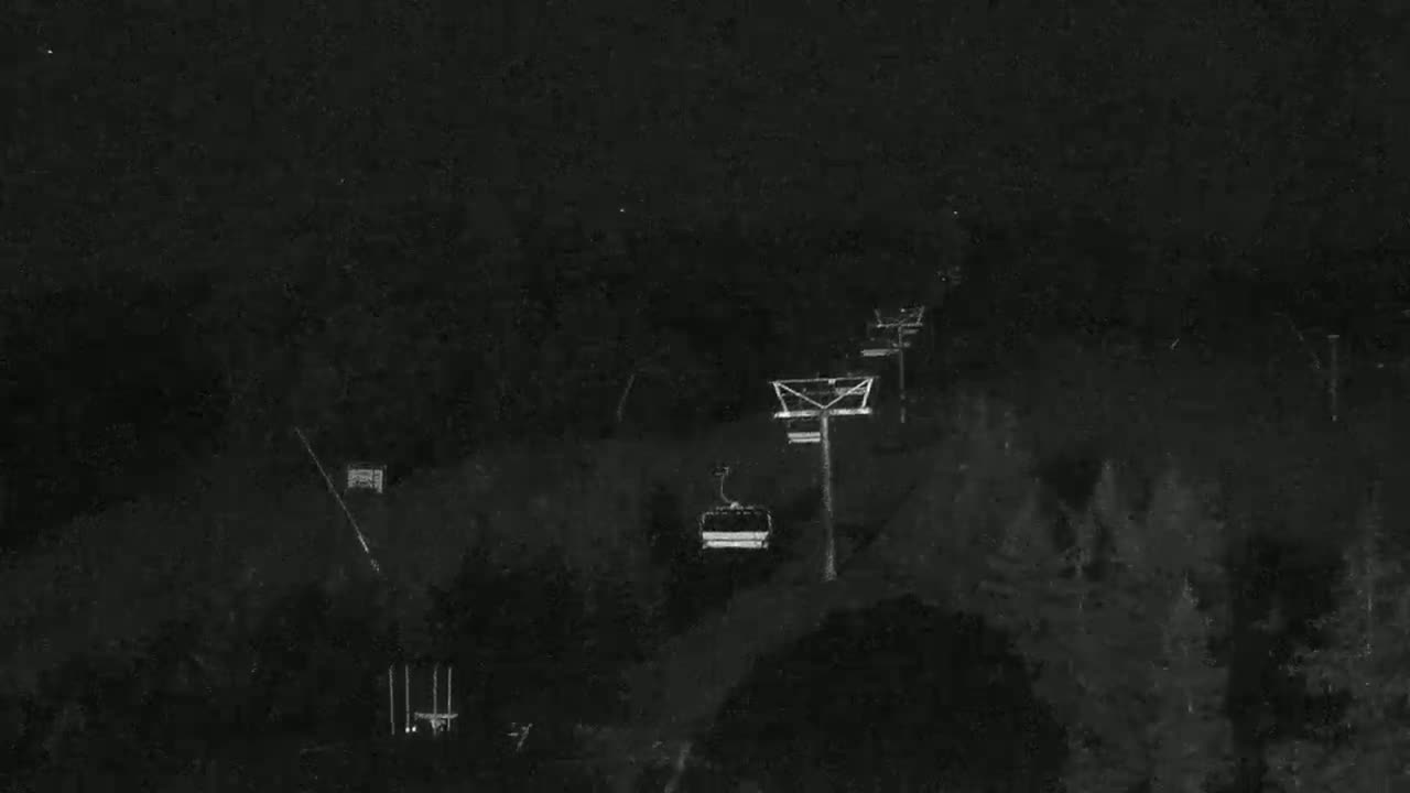 A chairlift ascends a dark, nighttime mountain slope covered in trees.
