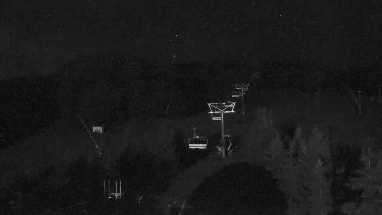 A chairlift ascends a dark, tree-covered hillside at night under a clear, starry sky.