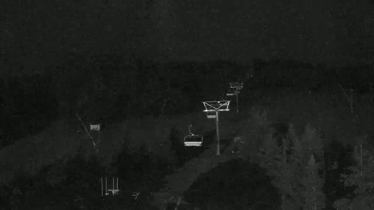 A chairlift carrying a single passenger moves across a dark, wooded landscape at night.