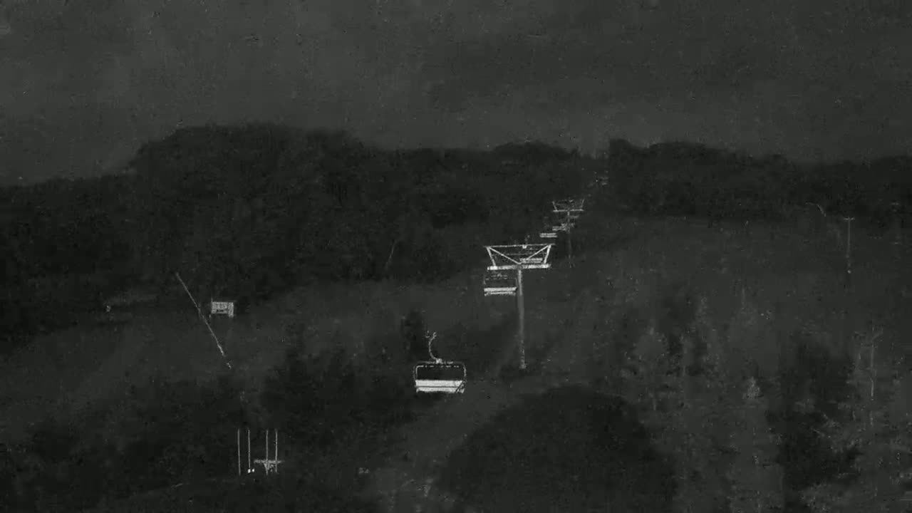 A chairlift ascends a dark, wooded hillside under a cloudy, nighttime sky.