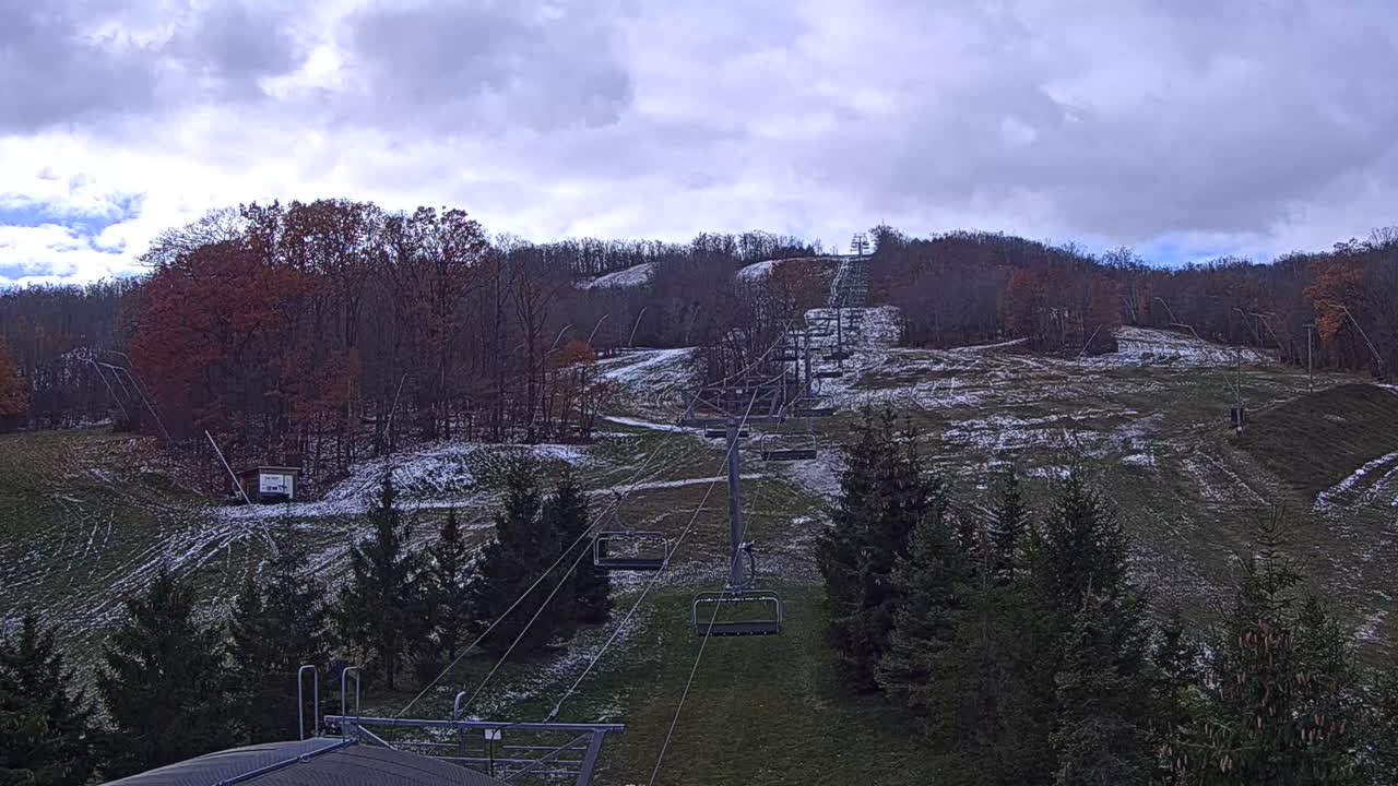 A chairlift carrying a single passenger moves along a track through a hazy, sunlit landscape of trees and open fields.