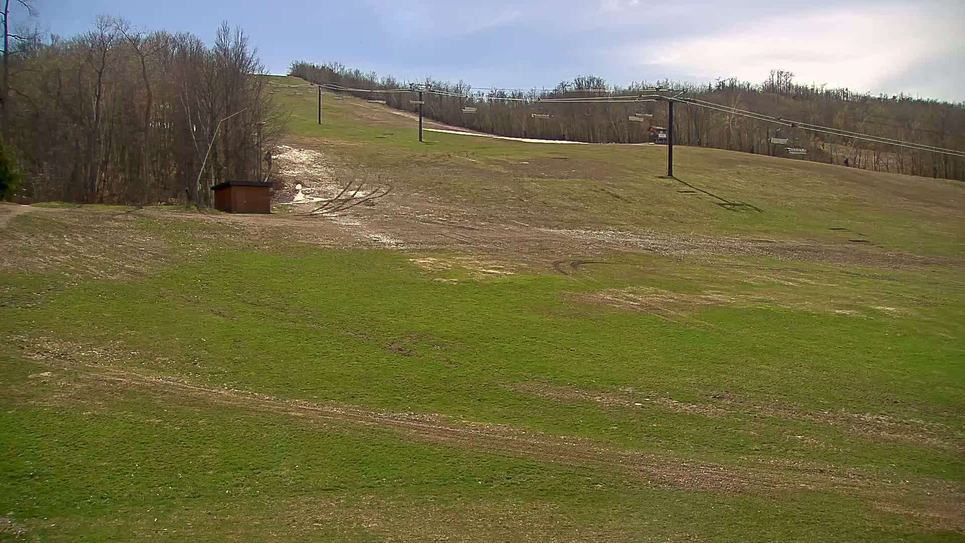 A grassy hill with a ski lift and a small building, under a partly cloudy sky.